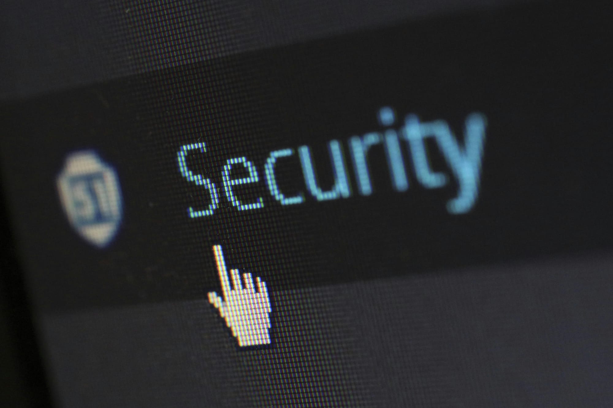 A computer screen displays the word "Security" in blue text, with a pixelated hand-shaped cursor pointing to it. The background is dark.
